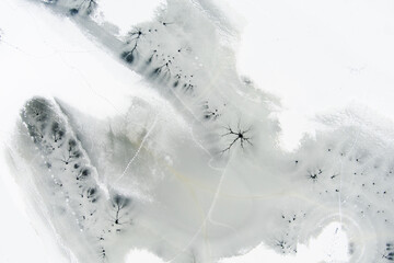 Aerial top-down winter view of frozen lake surface, ice texture with cracks, underwater streams spots.