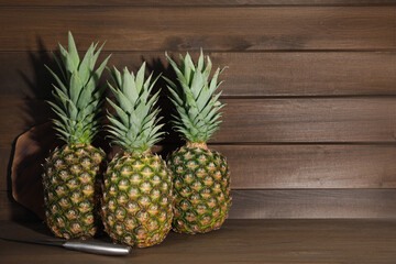 Whole ripe pineapples and knife on wooden table. Space for text