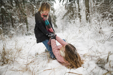 Funny teen sisters having fun on a walk in snow covered pine forest on chilly winter day. Teenage girls exploring nature.