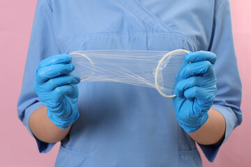 Doctor with unrolled female condom on pink background, closeup. Safe sex