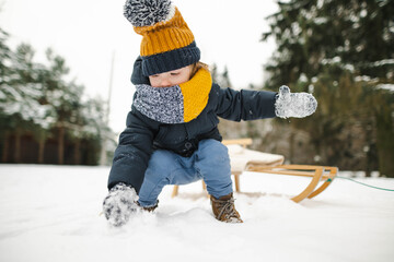 Funny toddler boy having fun with a sleigh in beautiful winter park. Cute child playing in a snow.