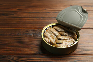 Open tin can of sprats on wooden table. Space for text