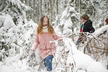 Funny teen sisters having fun on a walk in snow covered pine forest on chilly winter day. Teenage girls exploring nature.