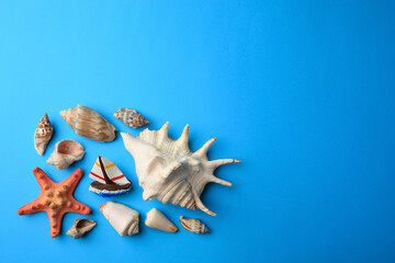 Obraz premium Beautiful starfish, decorative ship and shells on blue background, flat lay. Space for text
