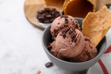 Tasty ice cream with chocolate chunks and piece of waffle cone in bowl on white table, closeup. Space for text