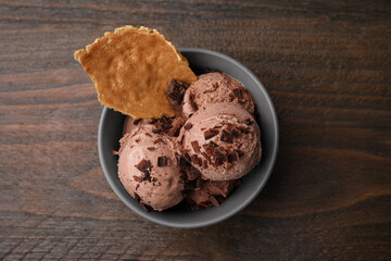 Tasty chocolate ice cream and piece of waffle cone in bowl on wooden table, top view