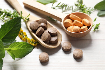 Different pills, herbs and flowers on white wooden table, closeup. Dietary supplements