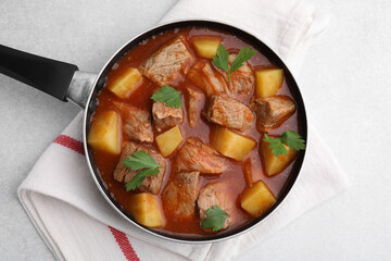 Delicious goulash in saucepan on light grey table, top view