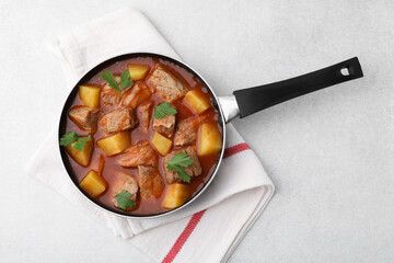 Delicious goulash in saucepan on light grey table, top view