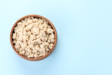 Tasty boiled oatmeal in bowl on light blue background, top view. Space for text