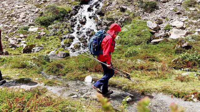 Trekkers couple backpackers with trekking poles slow motion crossing Mountain creek running down in Makalu Barun National Park near Kothe settlement. Mera peak climbing route, Himalayas, Nepal.