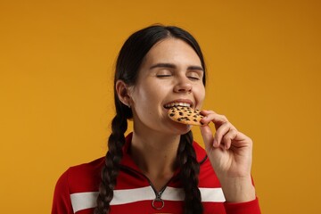 Young woman with chocolate chip cookie on orange background