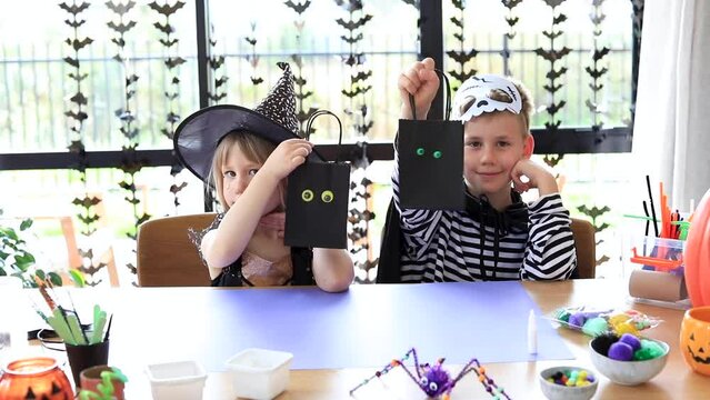 Cute brother and sister in Halloween costumes are doing festive crafts. 