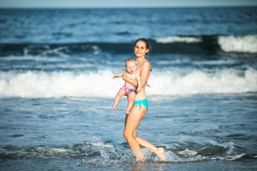 mother hugging her baby boy at the ocean wave. Concept of union and tender connection between a young mama and his lovely child.