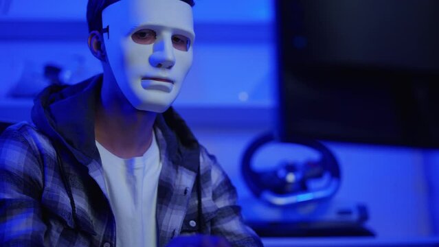 Short of computer hacker wearing white mask stealing data from a laptop.