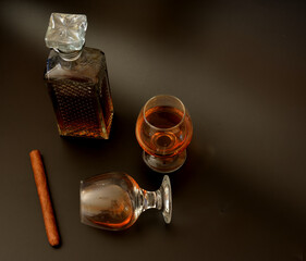 A crystal decanter and two glasses of cognac next to a cigar on a black background.