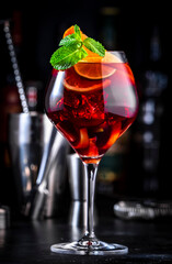 Red sangria cocktail drink with tempranillo wine, peach, plum, orange, lime and ice. Black bar counter background, steel bar tools and bottles