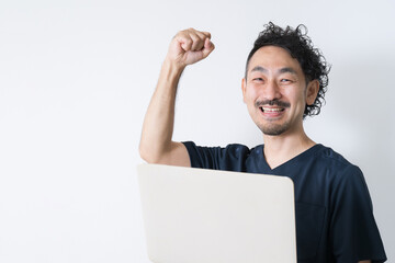 ノートパソコンを持ってガッツポーズをする男性　整体や看護師、ドクターのイメージ　カメラ目線左にコピースペースあり