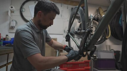 Man bicycle mechanic installs cycle chain on bike. Technician fixes bicycle chain gear at bicycle repair shop. Bicycle mechanic adjusts bike chain. Mechanical engineer fixing transmission in workshop