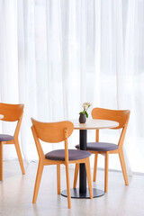 Wooden coffee table set with little ceramic vase near white curtain inside of modern coffee shop in beige tone style and vertical frame