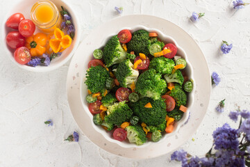 table with violet flowers and a vegan salad with pieces of broccoli, tomato, pickles and carrot.