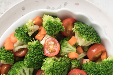 White wooden table with a vegan salad with pieces of broccoli, tomato, pickles and carrot.