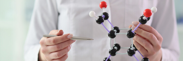 Woman chemist points pen to molecule model holding in hand