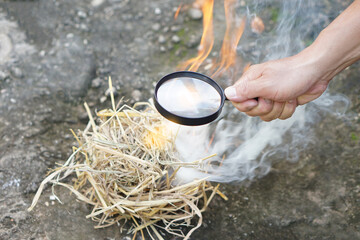 Close up hand held magnifying glass to make fire for burning dried hays. Concept, Science...