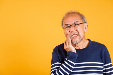Dental pain. Asian unhappy elder man problems with gum pain studio shot isolated on yellow background, Portrait senior old man sad hand touching cheek suffering from toothache, dental healthcare - obrazy, fototapety, plakaty