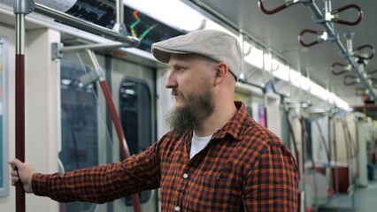 Bearded man holds handrail in public transport. Dynamic video of serious millennial man in cap are...