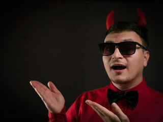 brunette man in a red shirt with a black bow tie in a black hat with red horns as a devil on a dark...