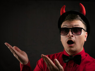 brunette man in a red shirt with a black bow tie in a black hat with red horns as a devil on a dark background cinematic lighting