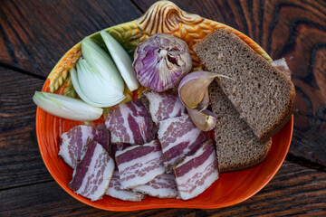 Appetizing lard pieces with garlic, onion and bread on a plate on a wooden table. Traditional snack...