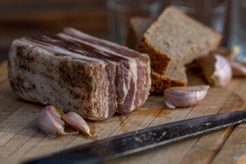 An appetizing piece of lard with garlic and bread on a wooden board. Traditional snack of Ukrainian and Russian cuisine. Close-up.