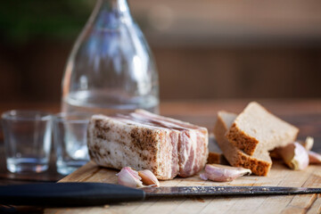 An appetizing piece of bacon with garlic and bread and a bottle of alcohol on a wooden board. Traditional snack of Ukrainian and Russian cuisine. Close-up.