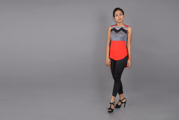 Fototapeta premium Studio shot of a young, beautiful Indian female model in casual wear wearing red and grey designer top and black jeans against white background. Female model. Fashion Portrait.
