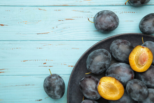 A plate of fresh blue plums on blue wooden background. - Powered by Adobe