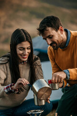 Diverse duo cooking noodles outdoors by a peaceful lake at their campsite