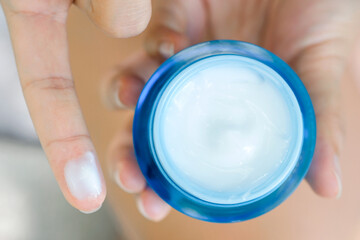 Hand of woman holding moisturizer cream and serum. She applying a facial cream , essential , oil ,...