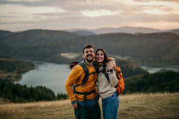 Two friends walking uphill with backpacks, catching sight of a serene lake