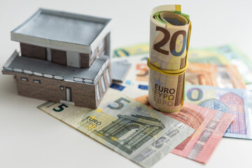 A toy house made of wood with a roof costs money, on a hundred-dollar bill. Concept: mortgage, purchase, sale of real estate, rental housing.