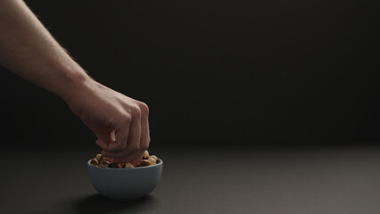 man take roasted hazelnuts from blue bowl on black paper background