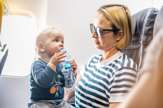 Mom and child flying by plane. Mother holding and playing with her infant baby boy child in her lap during economy comercial flight. Concept photo of air travel with baby. Real people