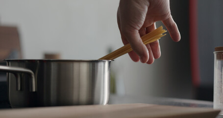 man hand put dried long fettuccine into saucepan with boiling water