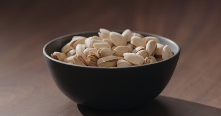 Roasted salted pistachios in black bowl on walnut table