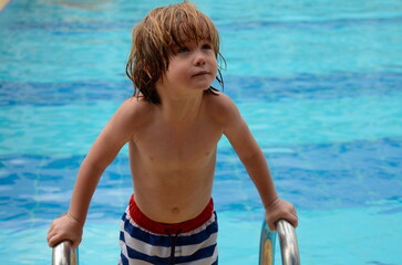 A little boy learns to swim in the pool. Child in swimming pool floating on inflatable mattress. Kids swim. Kid l having fun on family summer vacation in resort