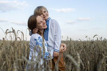 boy and a woman in embroidered shirts tenderly hug each other among the ears of corn in a wheat...