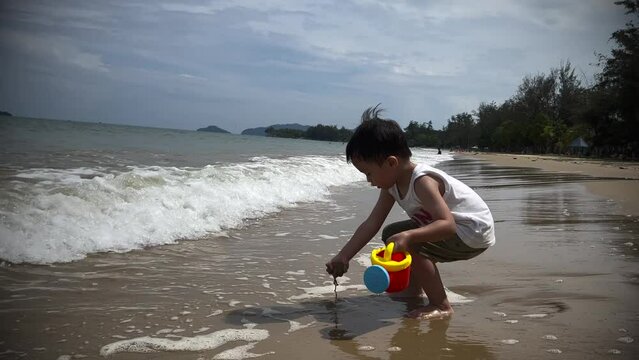 Happy 2-3 years old child enjoying playing on beach with splashing warm sea water