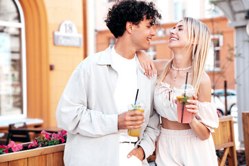 Young smiling beautiful woman and her handsome boyfriend in casual summer clothes. Happy cheerful family. Female having fun. Couple posing in street. Holding and drinking cocktail drink in plastic cup