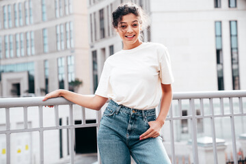 Young beautiful smiling hipster woman in trendy summer white t-shirt and jeans clothes. Carefree woman, posing in the street at sunny day. Positive model outdoors. Cheerful and happy